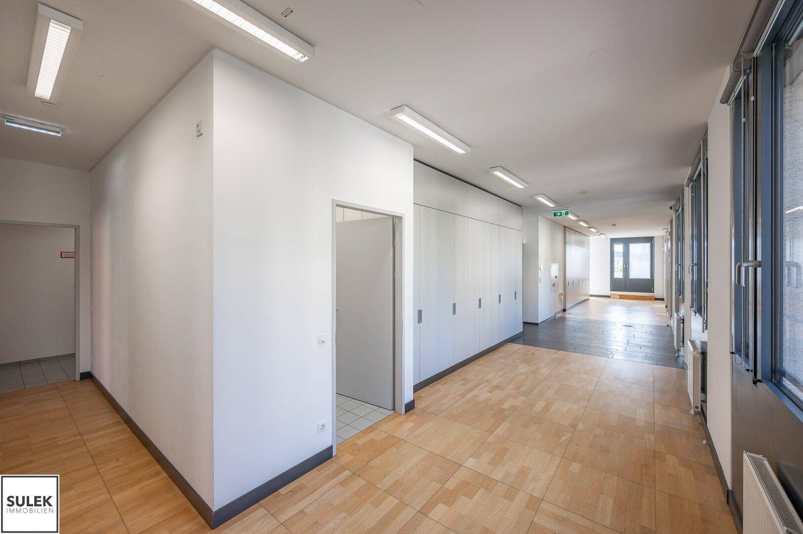 Geräumiger Flur mit Holzboden, weißen Wänden und Zugang zu Toiletten.