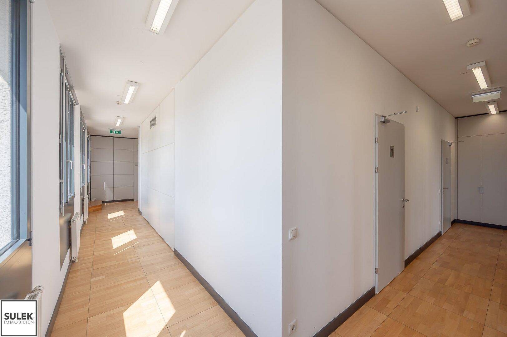 Langer, heller Flur mit Holzboden und Fenstern, die Tageslicht hereinlassen.
