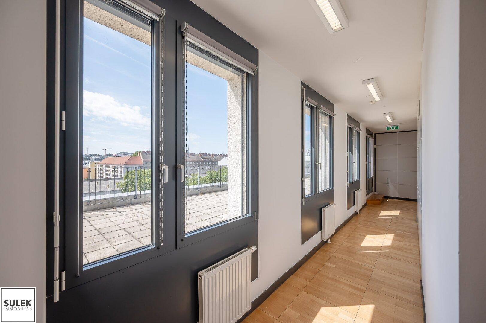 Heller Flur mit Holzboden und Fenstern, die einen Blick auf eine Dachterrasse bieten.