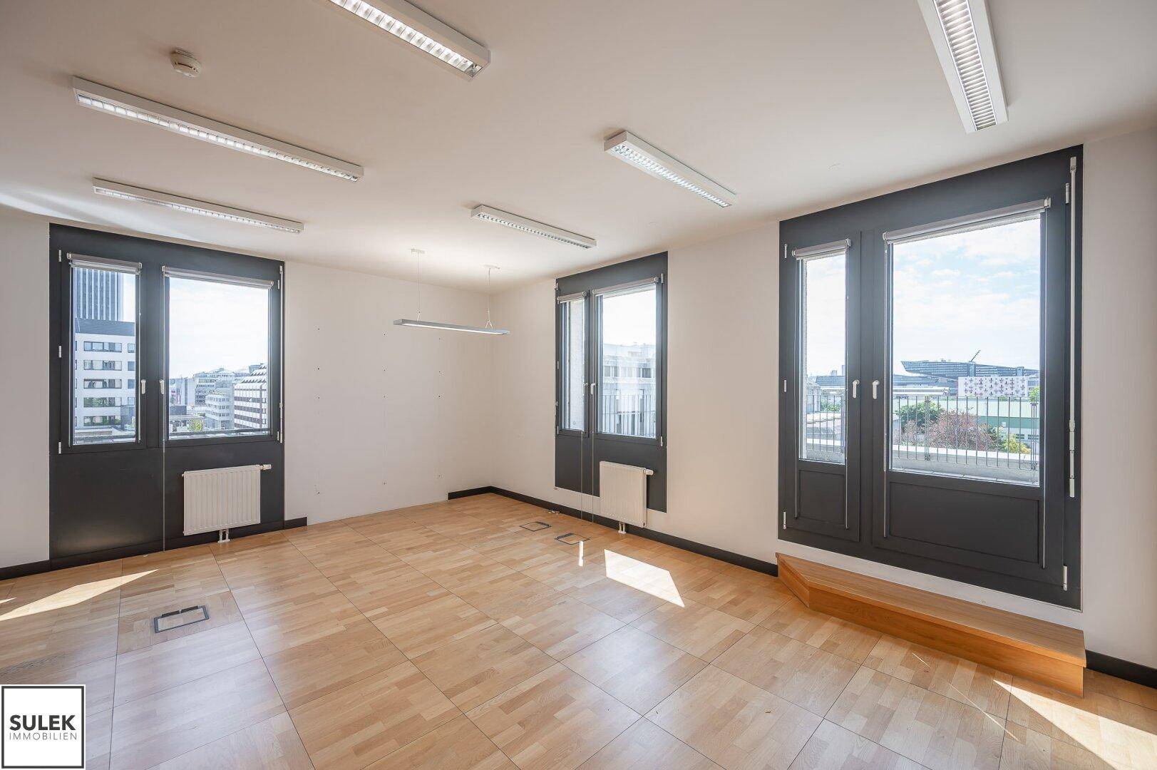 Geräumiger Büroraum mit Holzboden, großen Fenstern und Stadtblick.