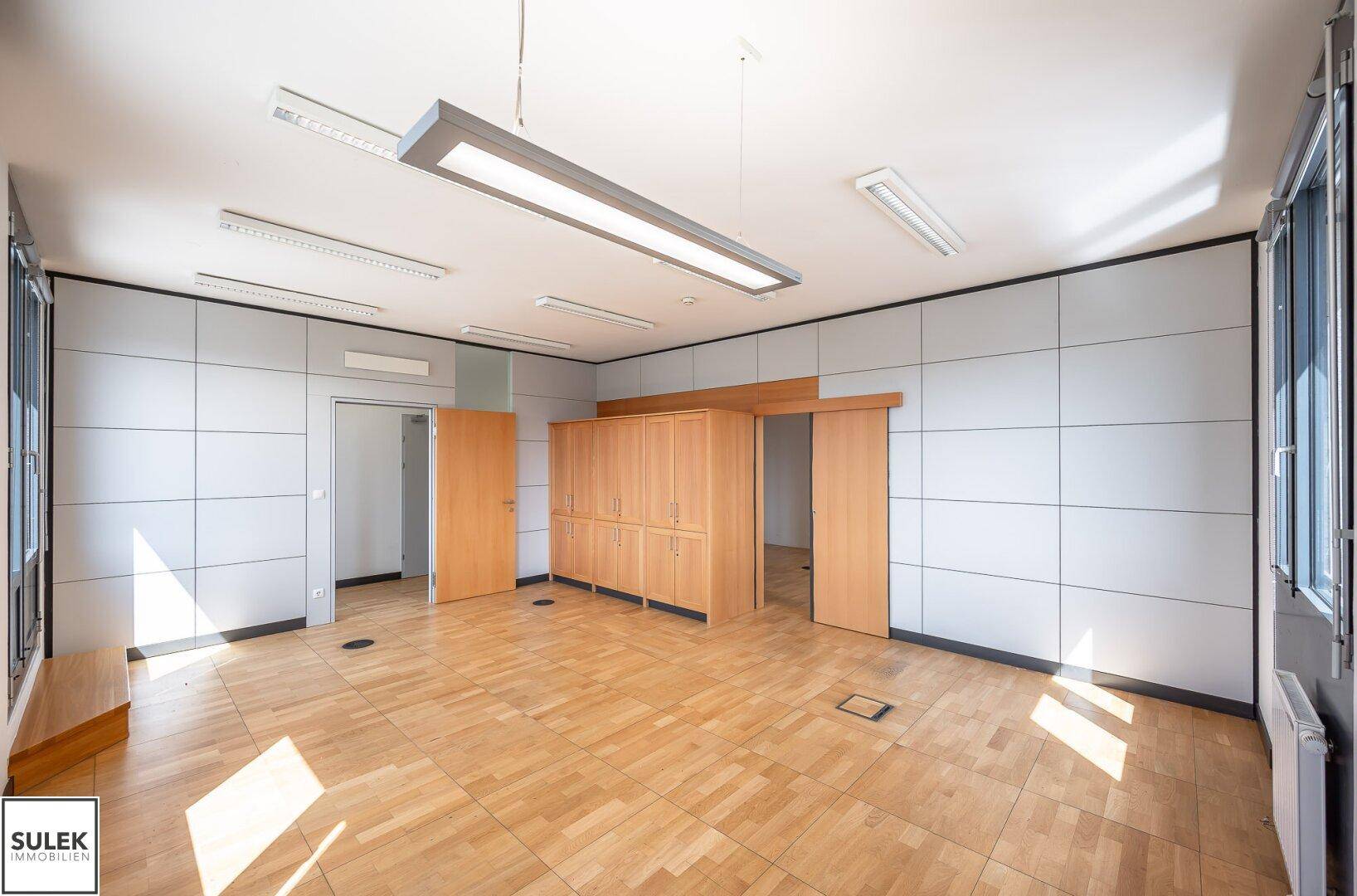 Heller Büroraum mit Holzboden, Einbauschränken und viel Tageslicht.