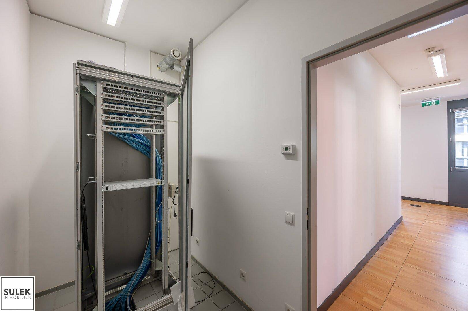 Serverraum mit offenem Rack und Verkabelung, angrenzend an einen Flur.
