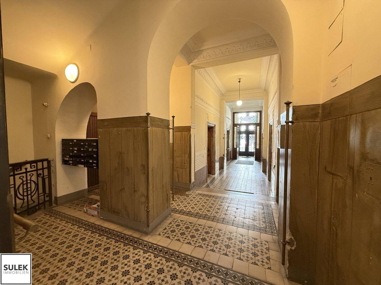 Langer, gewölbter Flur in einem Altbau mit gemustertem Fliesenboden und Briefkästen.