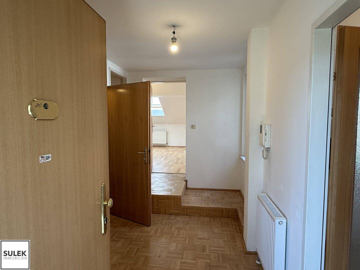 Eingangstür zur Wohnung, die in einen Flur mit Parkettboden führt.