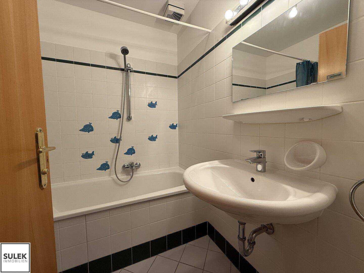 Badezimmer mit Badewanne, Waschbecken und weißen Fliesen mit blauen Dekorationen.