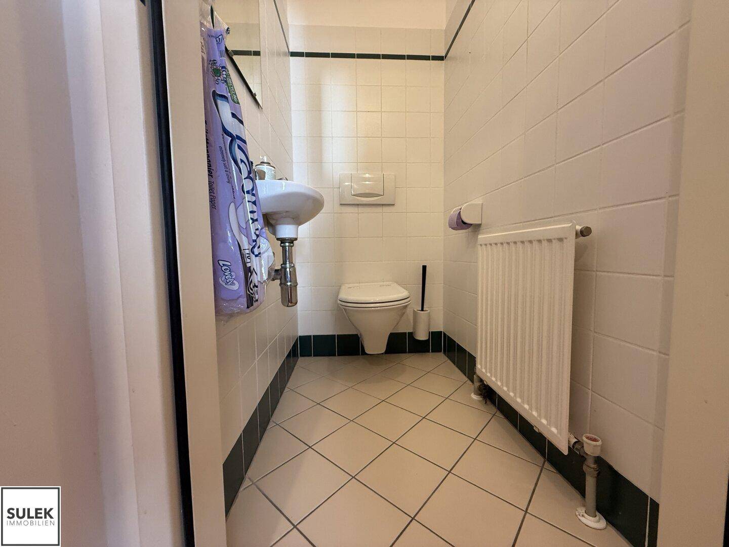 Kleines Gäste-WC mit weißen Fliesen, Waschbecken, Toilette und Heizkörper.