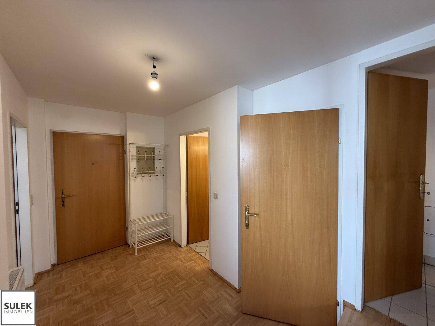Einfacher Eingangsbereich mit Parkettboden, mehreren Holztüren und einem Schuhregal.