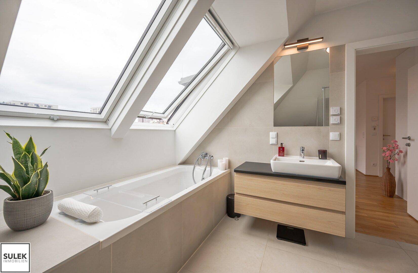 Modernes Badezimmer mit Badewanne unter Dachfenstern und stilvollem Waschtisch.