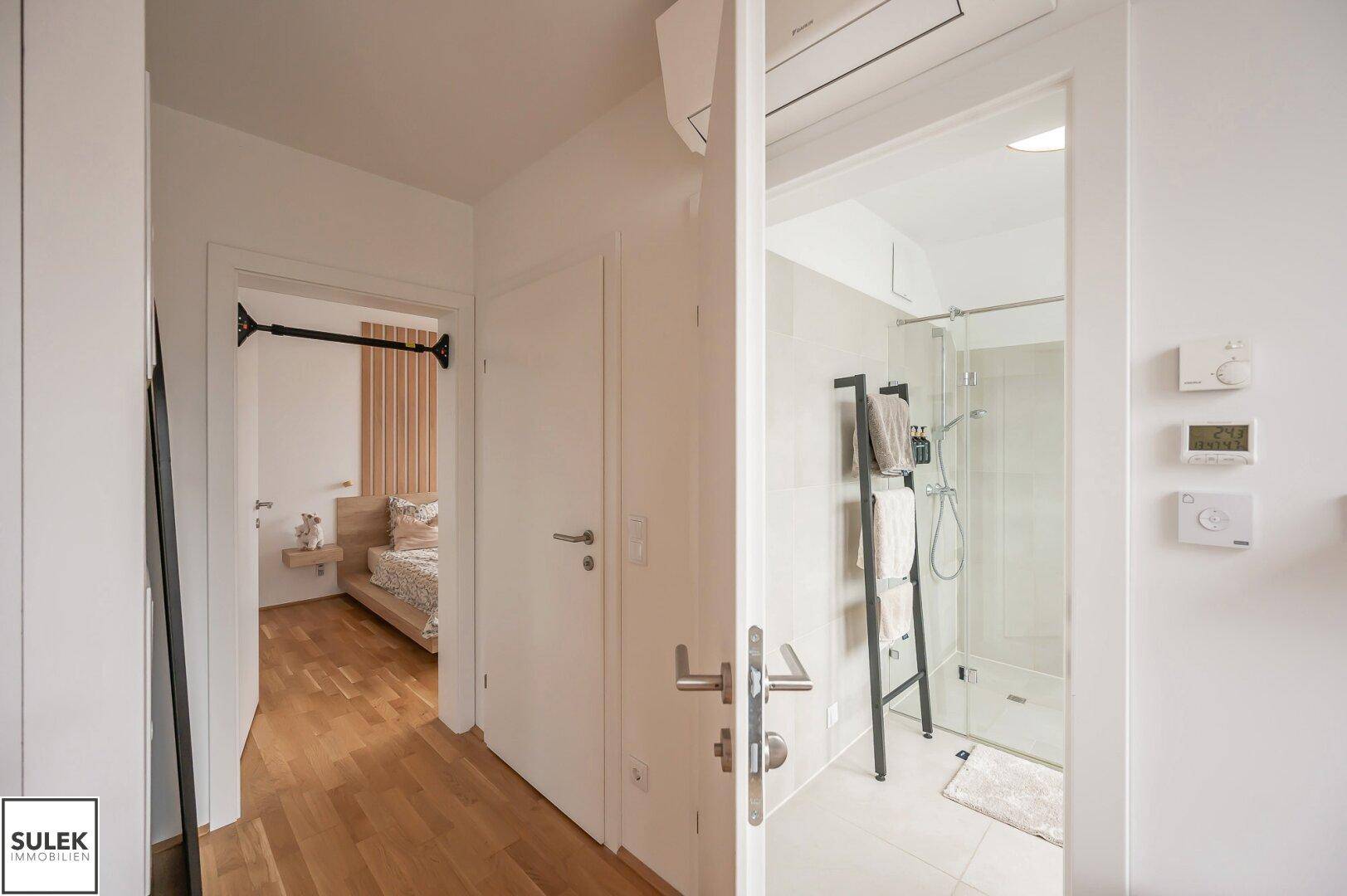 Flur mit Zugang zu Schlafzimmer und modernem Badezimmer mit Dusche.