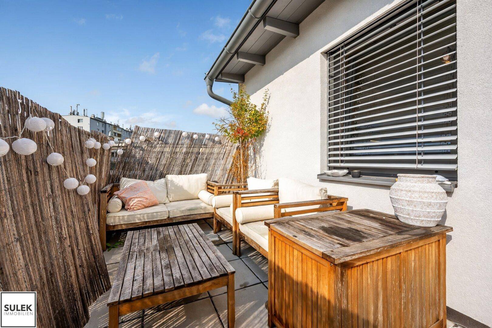 Gemütlicher Lounge-Bereich auf der Terrasse mit Holzsitzmöbeln und dekorativer Beleuchtung.
