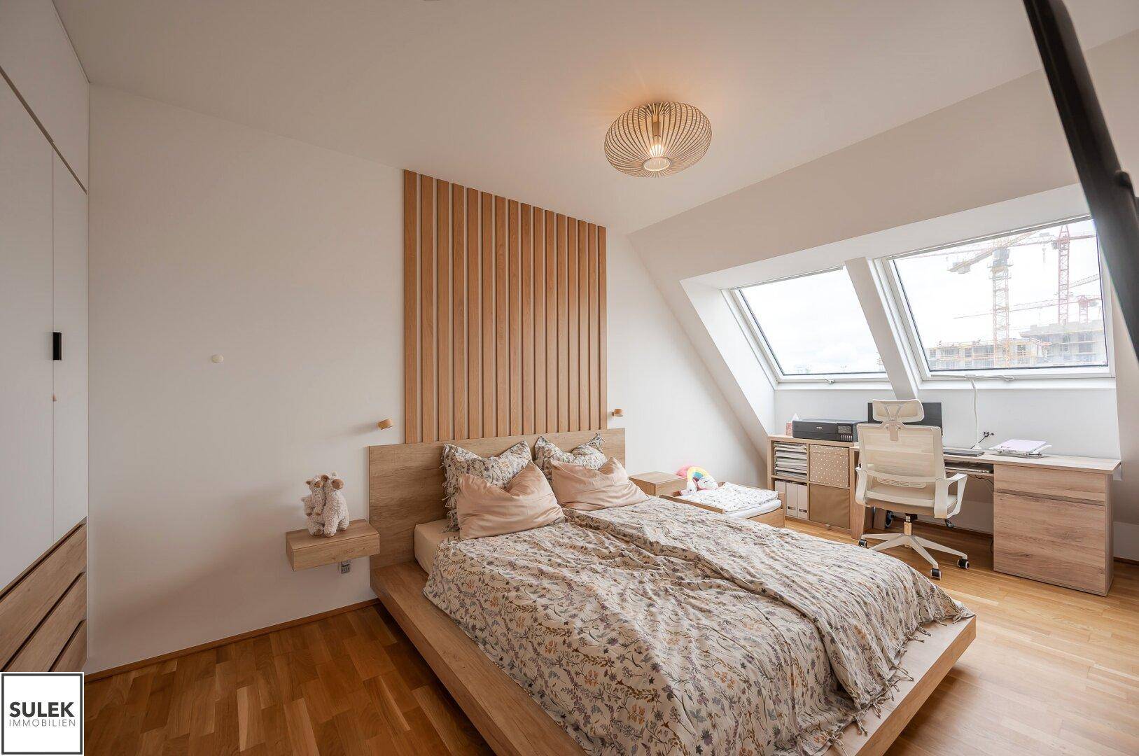 Helles Schlafzimmer mit Schreibtischbereich unter Dachfenstern und modernem Holzbett.
