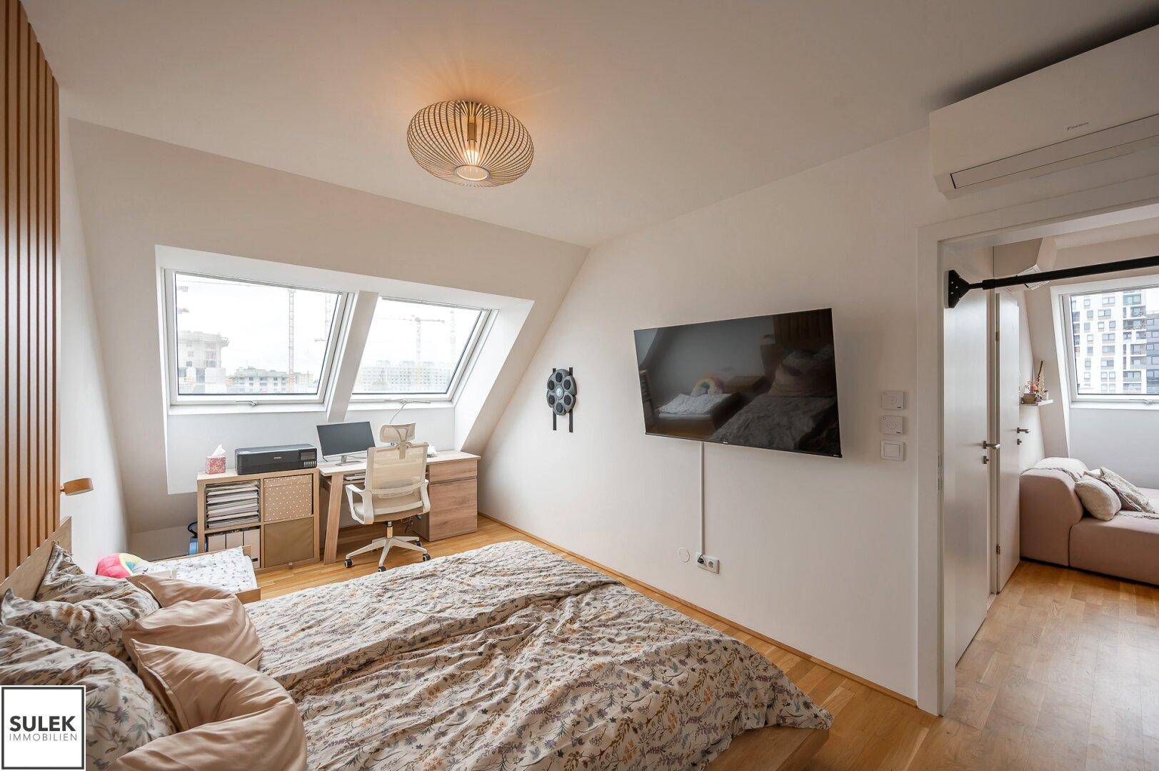 Gemütliches Schlafzimmer mit Arbeitsbereich unter Dachfenstern und Holzboden.