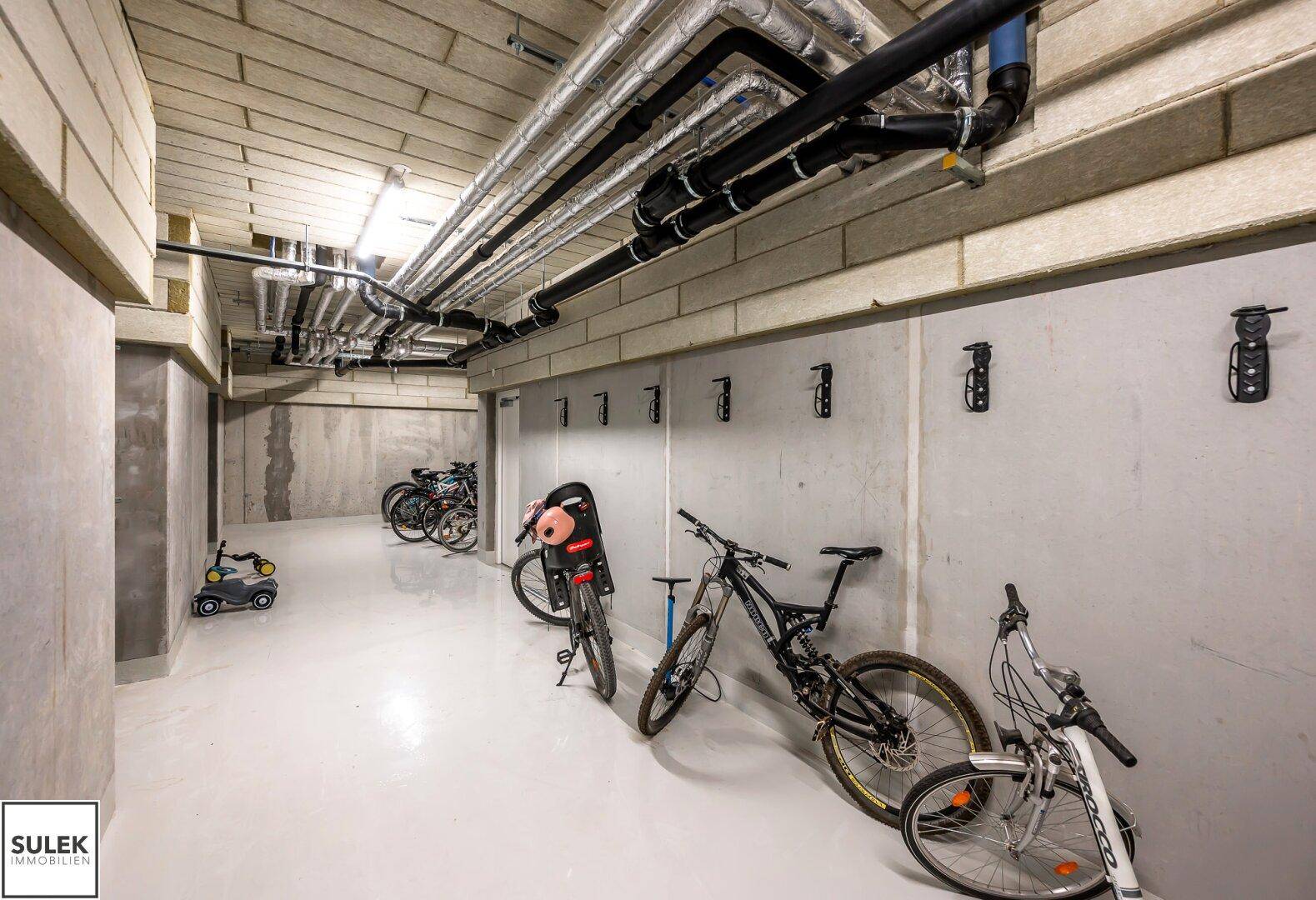 Geräumiger Fahrradraum im Untergeschoss mit sichtbaren Installationen und Abstellmöglichkeiten.