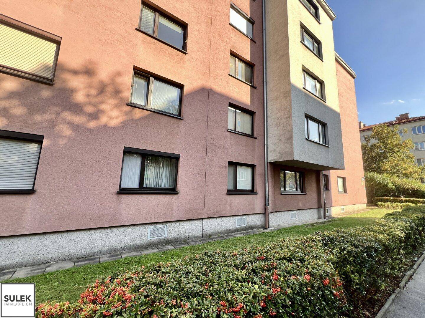 Fassade eines Wohnhauses mit Fenstern, einigen Rollläden und einer gepflegten Hecke im Vordergrund.