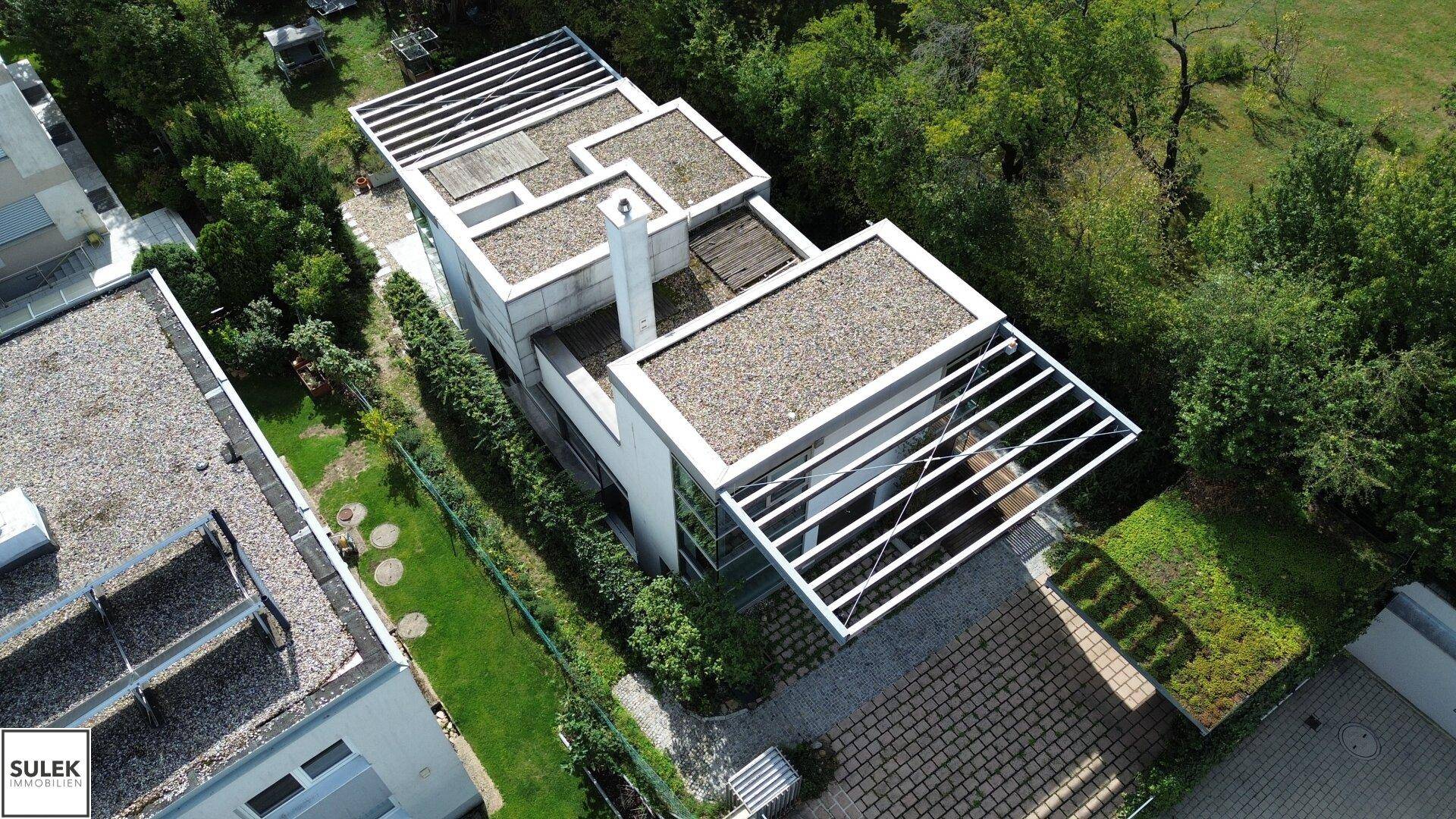 Moderne Architektur mit Flachdach und großen Fensterfronten, umgeben von viel Grün.