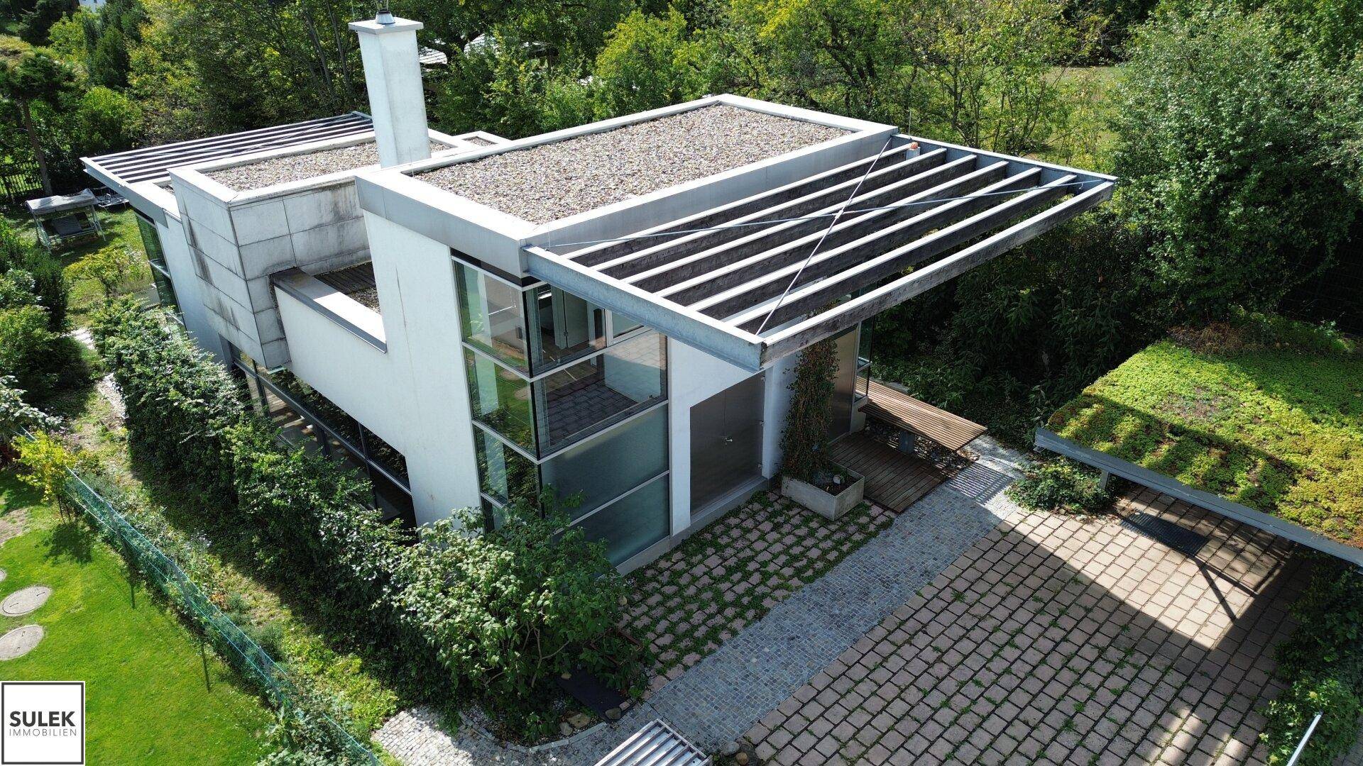 Vogelperspektive eines modernen Hauses mit Flachdach, Glasfassade und begrüntem Carport.