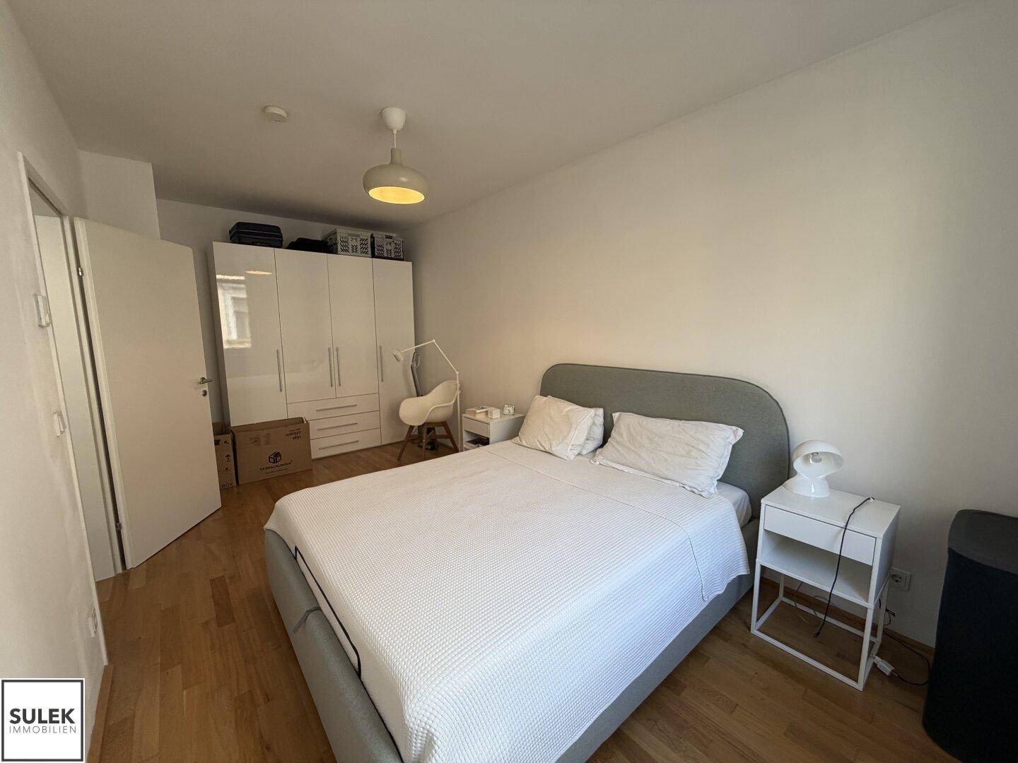 Helles Schlafzimmer mit Doppelbett, Holzfußboden und weißem Kleiderschrank.