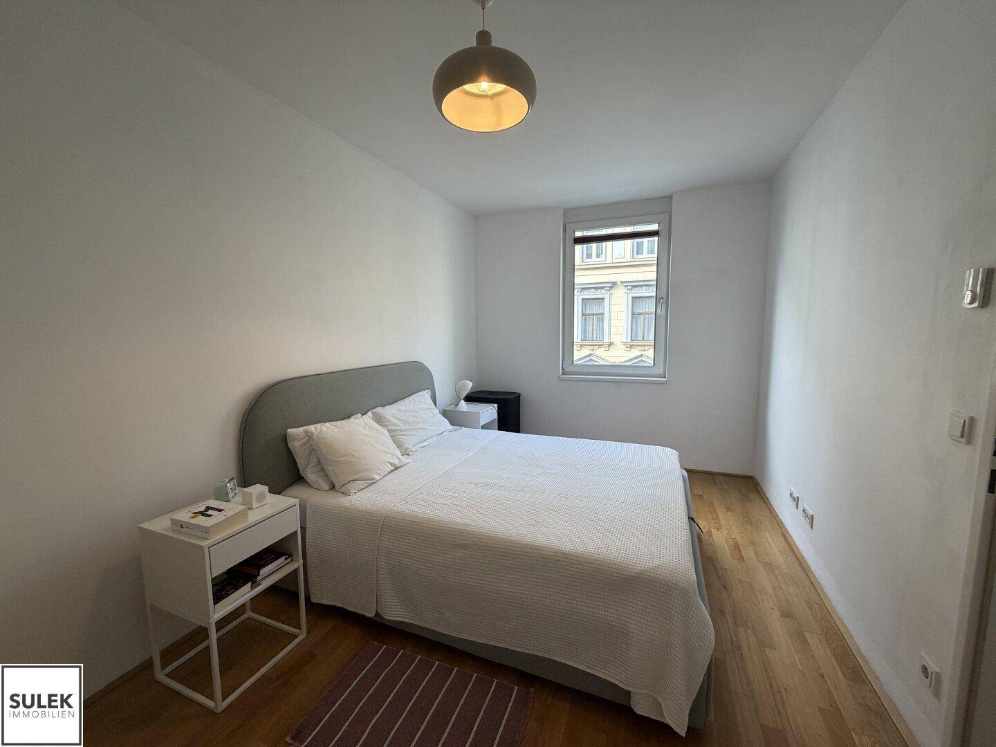 Gemütliches Schlafzimmer mit Doppelbett, Holzfußboden und Fenster mit Stadtblick.