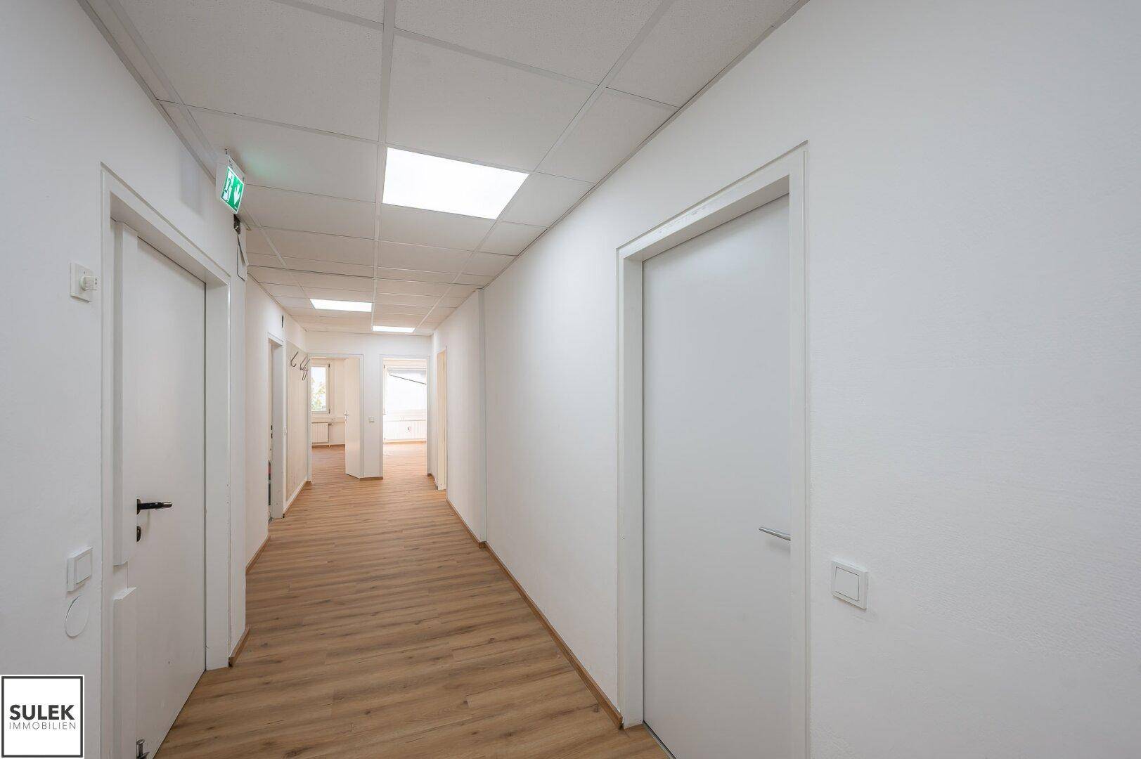 Heller Flur mit Laminatboden, weißen Wänden und Deckenbeleuchtung, der zu weiteren Räumen führt.
