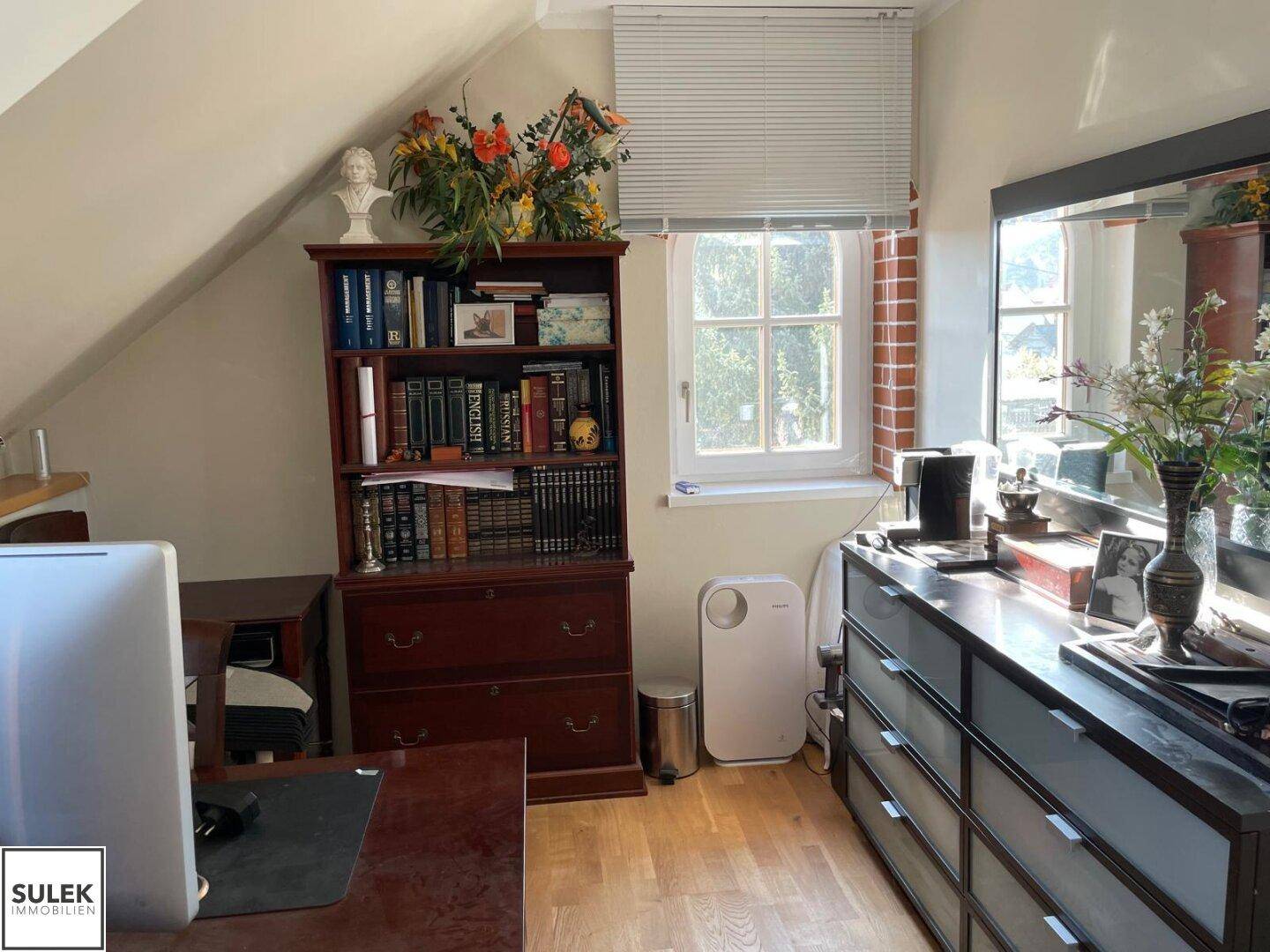 Gemütliches Arbeitszimmer im Dachgeschoss mit Holzboden, klassischem Bücherregal und Fenster.
