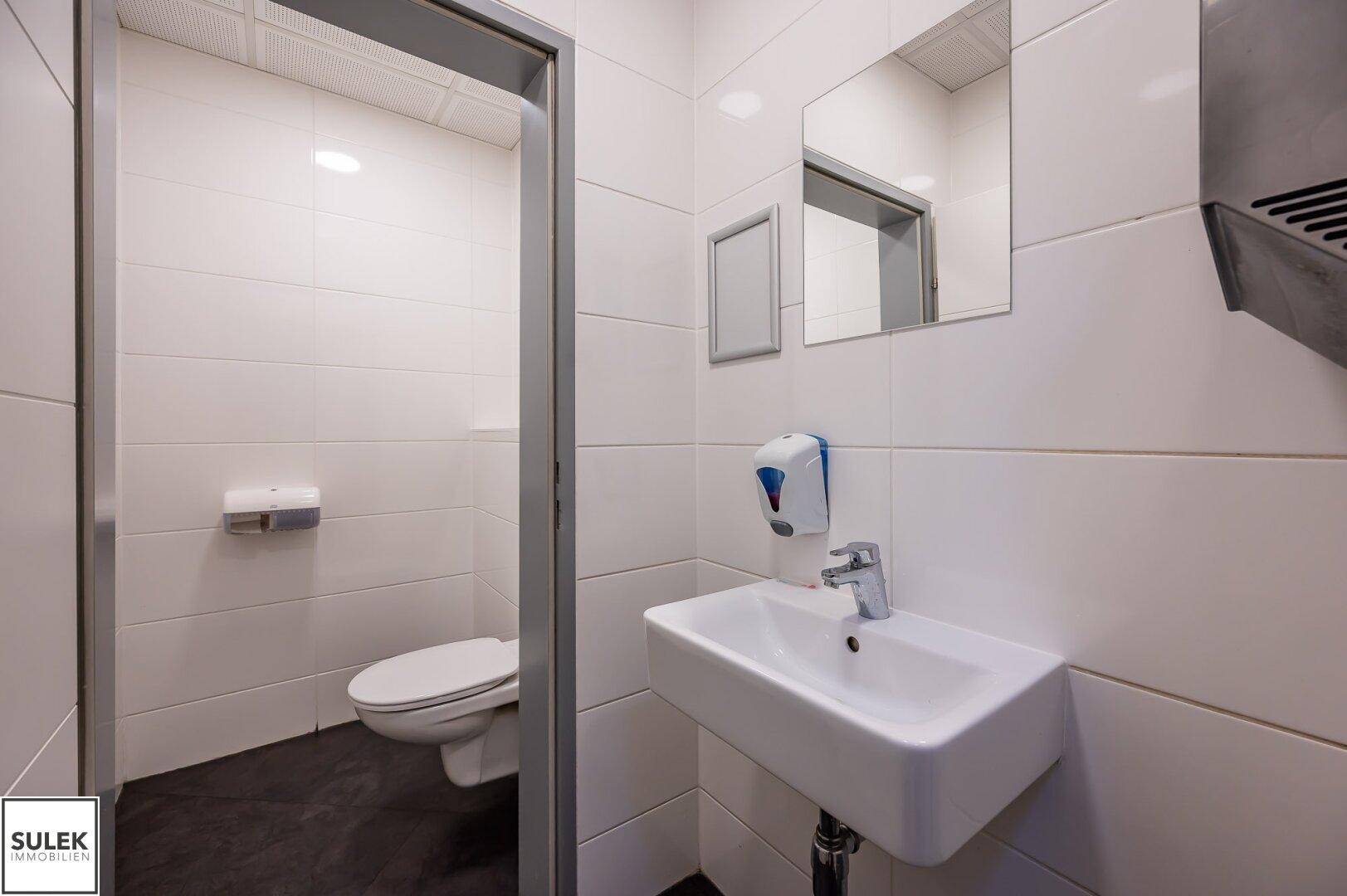 Kleiner Toilettenraum mit weißen Fliesen, Waschbecken und wandhängendem WC.