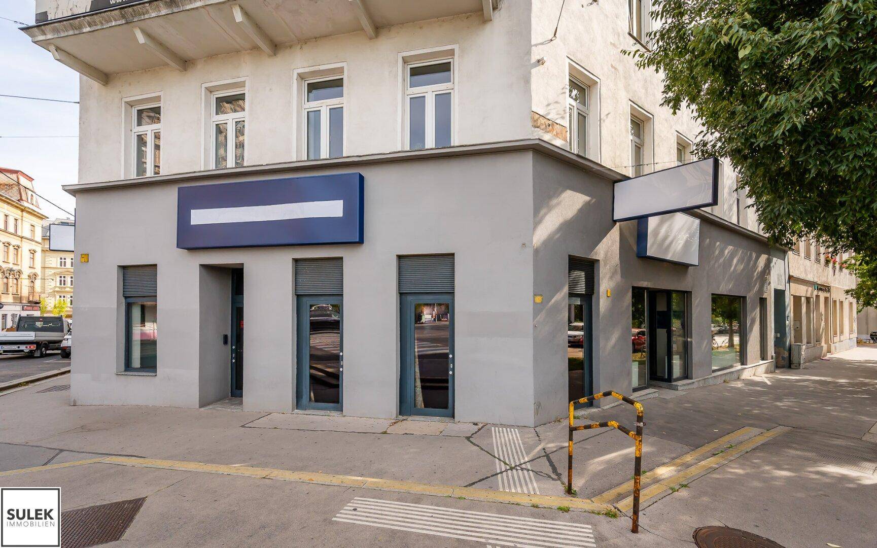 Außenansicht eines Eckgebäudes mit Ladenlokal im Erdgeschoss und geschlossenen Rollläden.