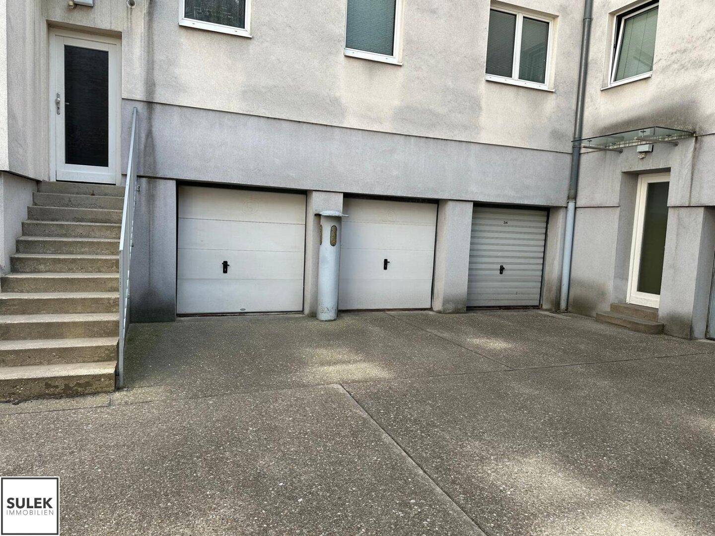 Außenansicht eines Gebäudes mit drei Garagentoren und einem Zugang über eine Treppe.