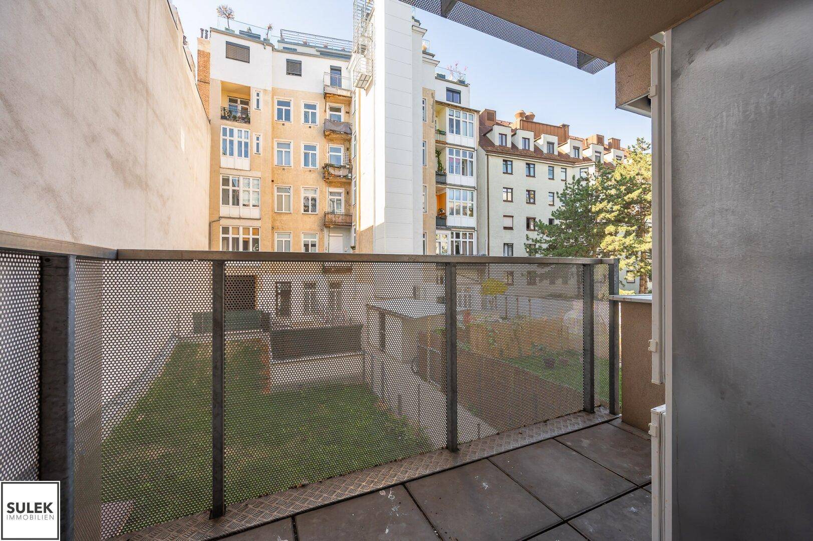 Balkon mit Metallgeländer und Blick auf den begrünten Innenhof und die umliegenden Gebäude.
