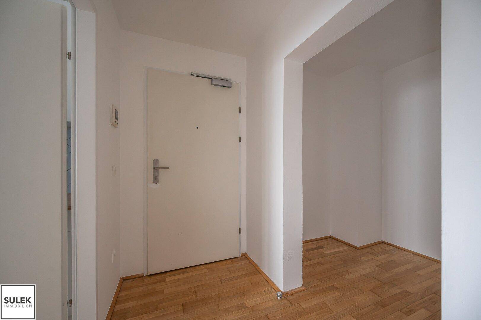 Eingangsbereich mit weißer Wohnungstür und hellem Parkettboden in einem gepflegten Zustand.