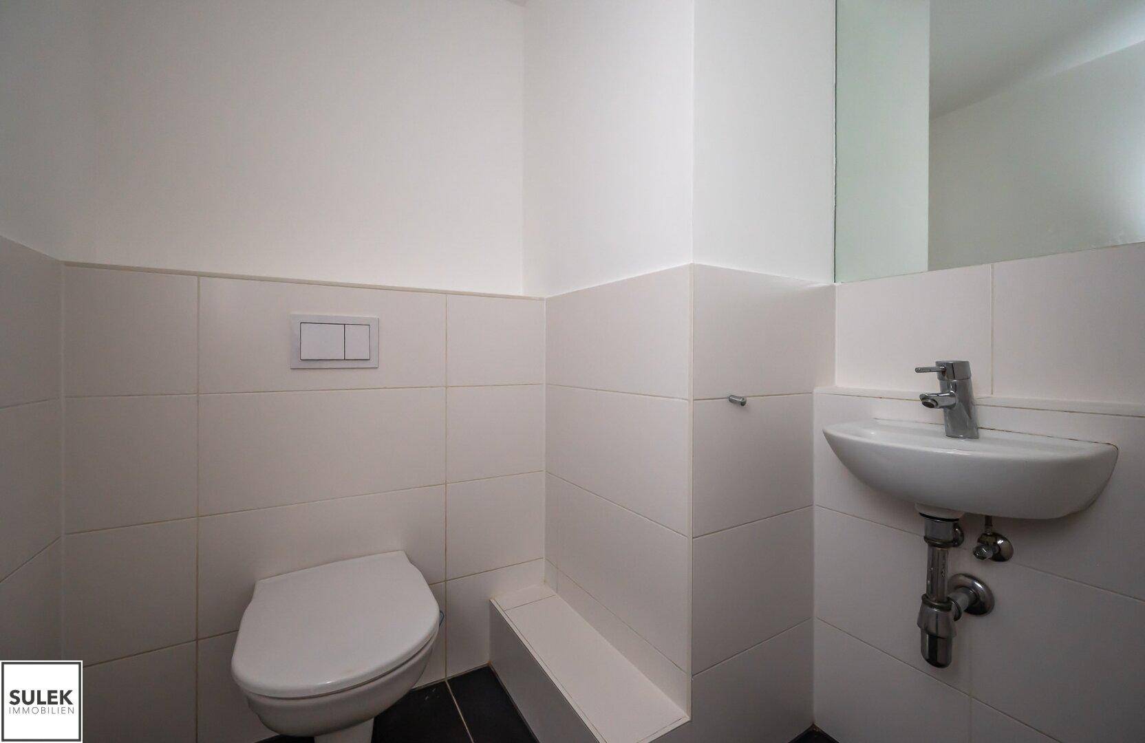 Separate Gästetoilette mit wandhängendem WC und kleinem Handwaschbecken in modernem Design.
