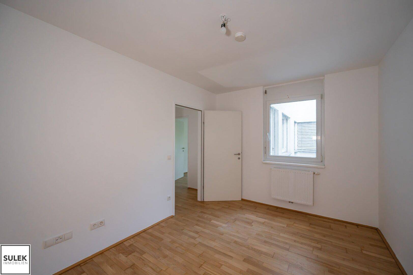 Ruhiges Zimmer mit Parkettboden und einem Fenster mit Jalousien, ideal als Schlaf- oder Arbeitszimmer.