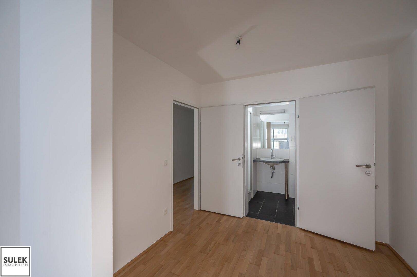 Helles Zimmer mit Parkettboden und direktem Zugang zu einem modernen Badezimmer.