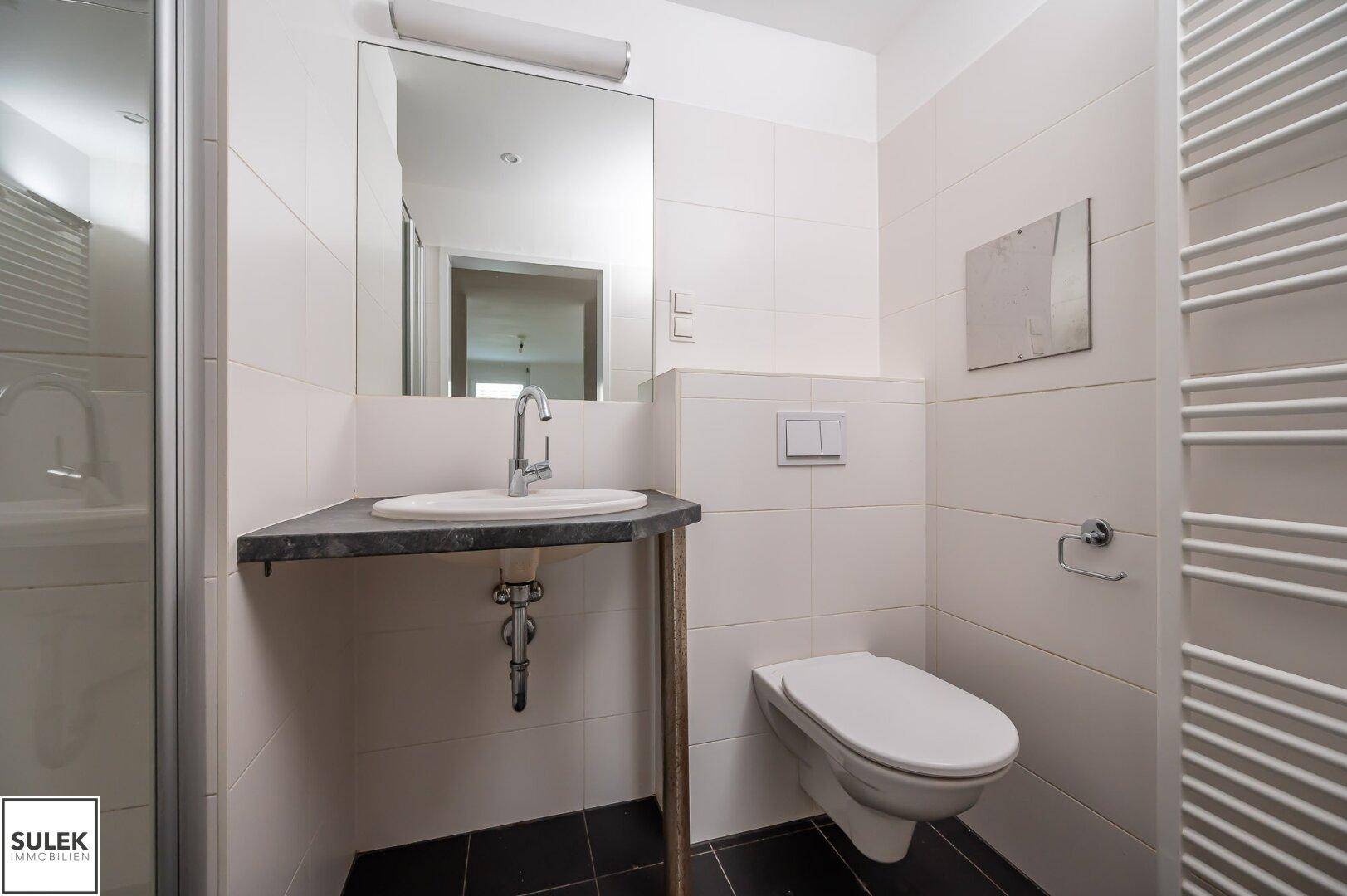 Modernes Badezimmer mit WC, Waschbecken und Duschbereich, ausgestattet mit weißen Fliesen.