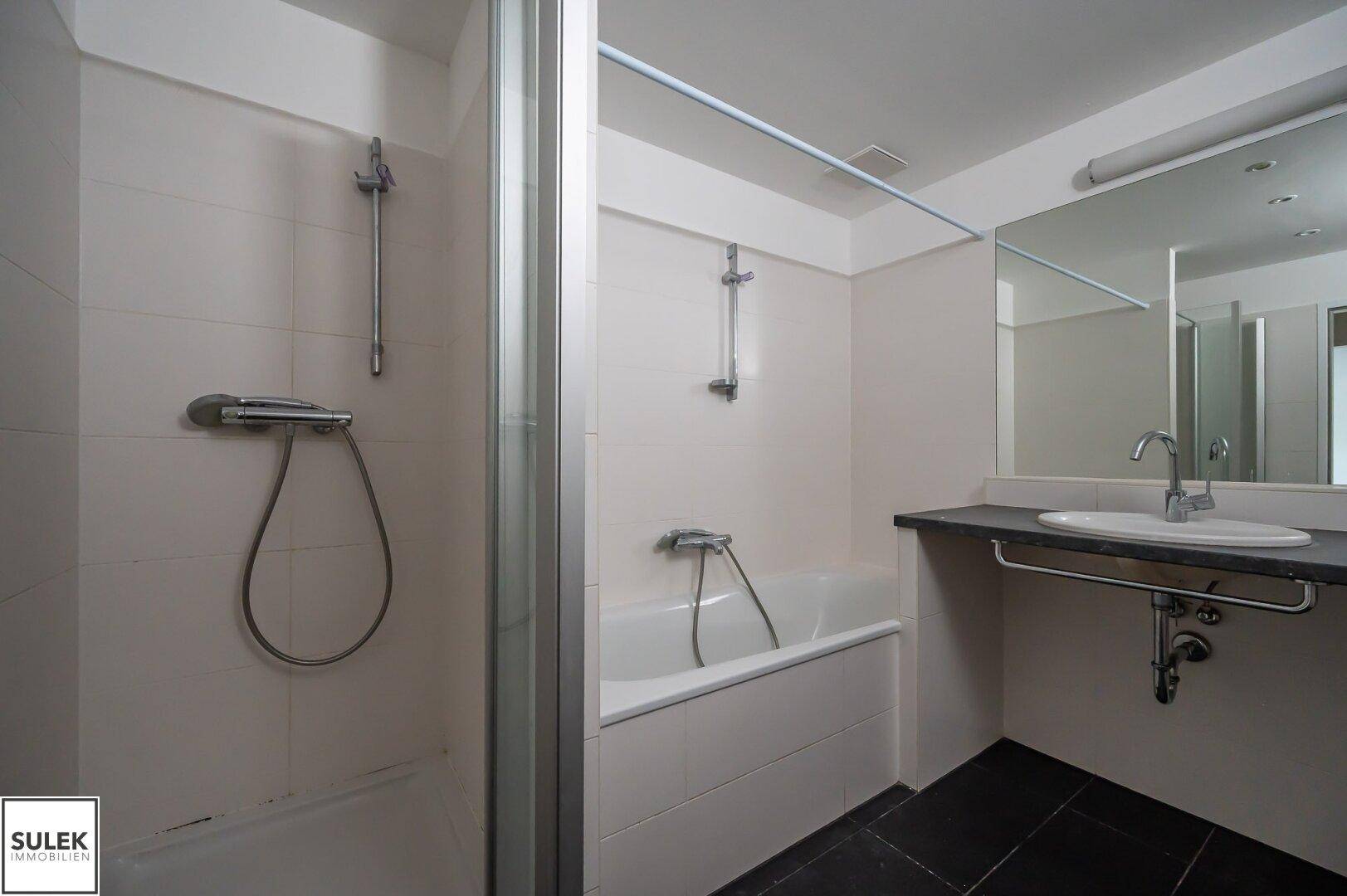 Badezimmer mit Badewanne, Waschbecken und Duschbereich, alles in hellen Fliesen gehalten.