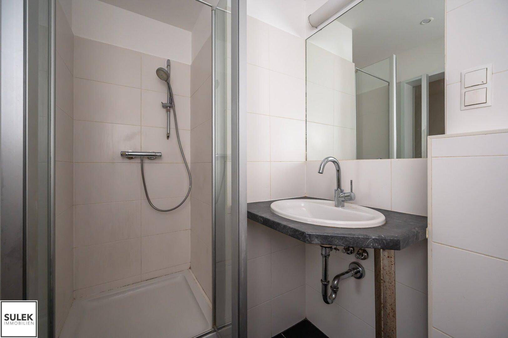 Modernes Badezimmer mit Duschkabine und Waschbecken, ausgestattet mit hellen Wand- und dunklen Bodenfliesen.