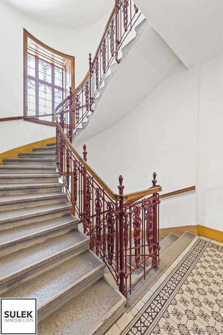 Wendeltreppe mit historischem Charme, verziertem Geländer und einem farbigen Bleiglasfenster.