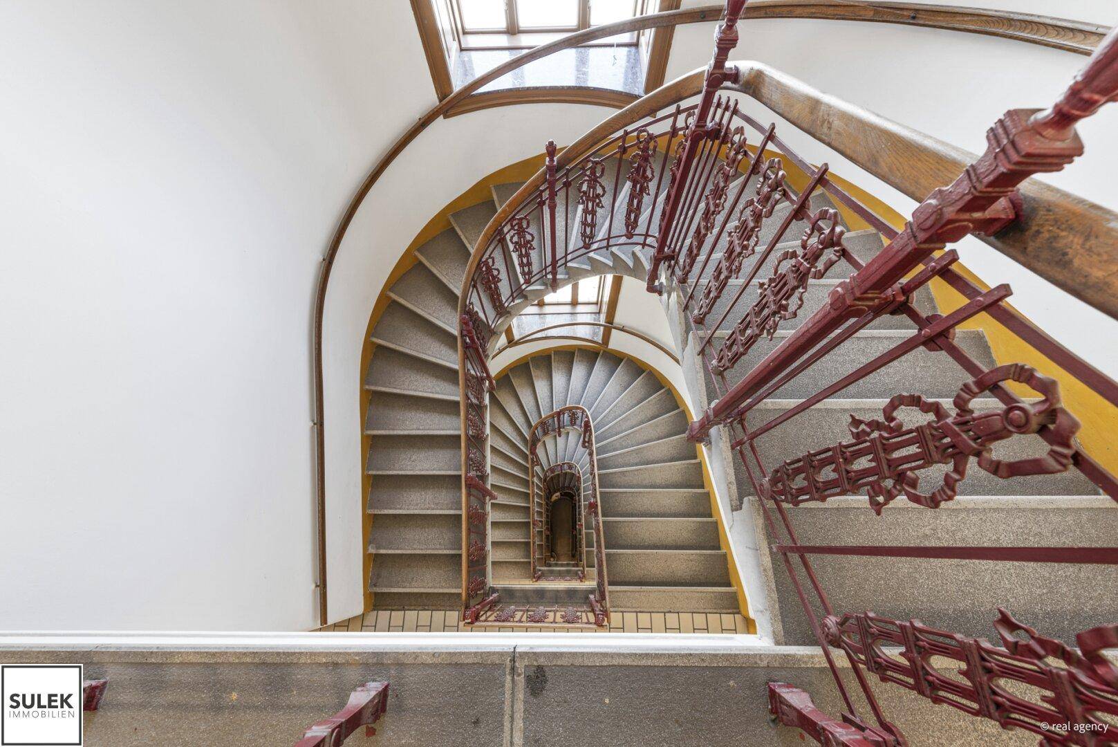 Blick von oben auf die kunstvolle Wendeltreppe, die sich spiralförmig durch das Treppenhaus windet.