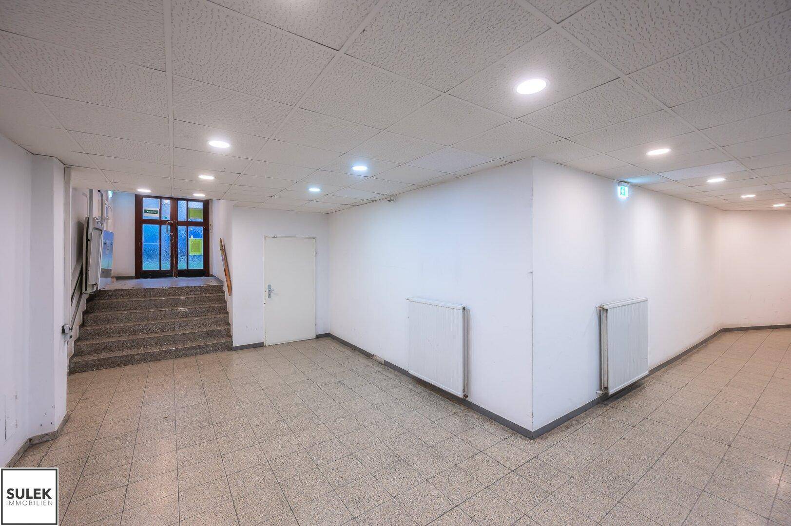 Heller Flur im Untergeschoss mit Fliesenboden, weißen Wänden und einer Treppe zum Ausgang.