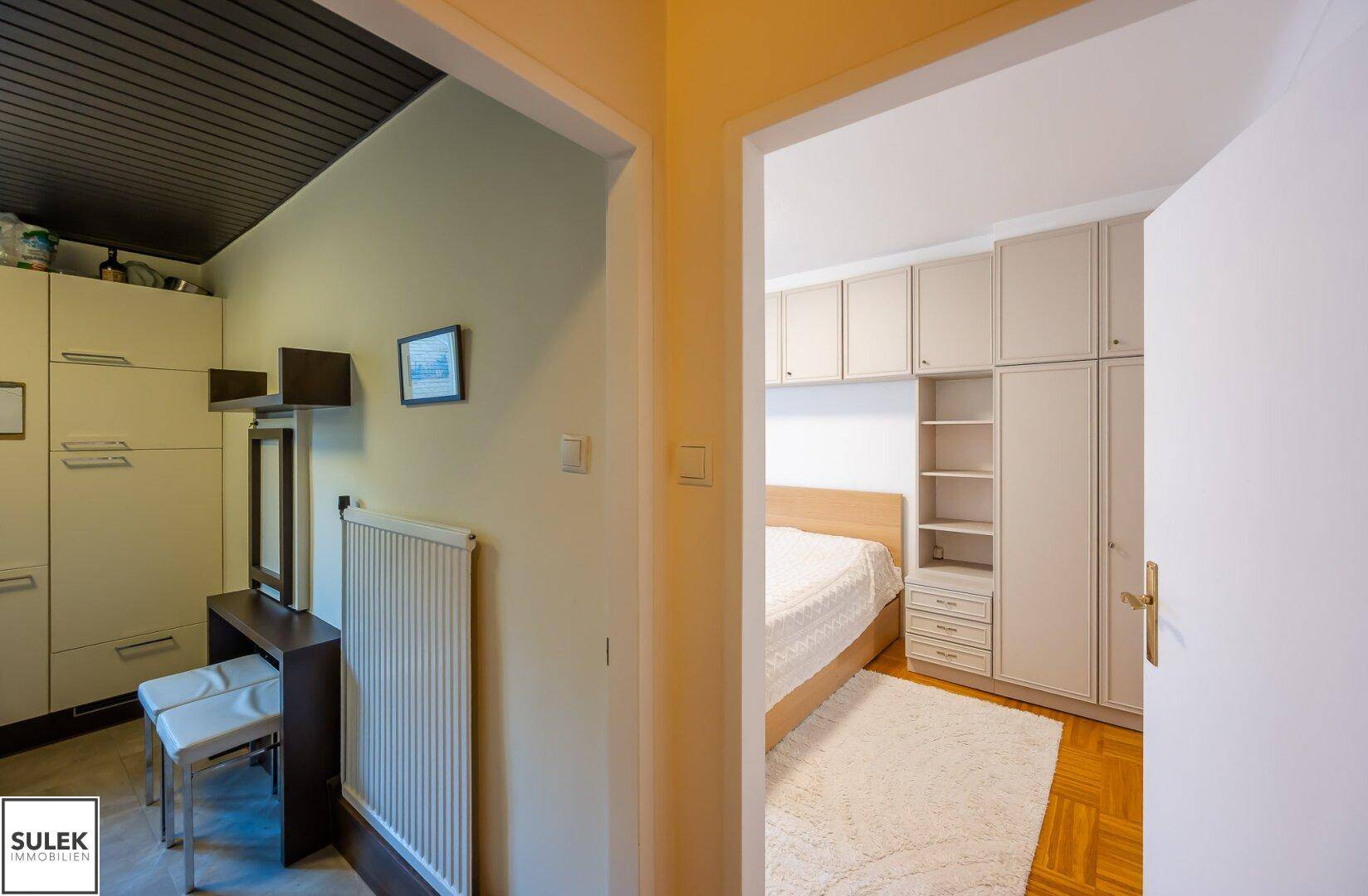 Eingangsbereich mit Heizkörper und Zugang zum Schlafzimmer, unter einer Holzdecke.