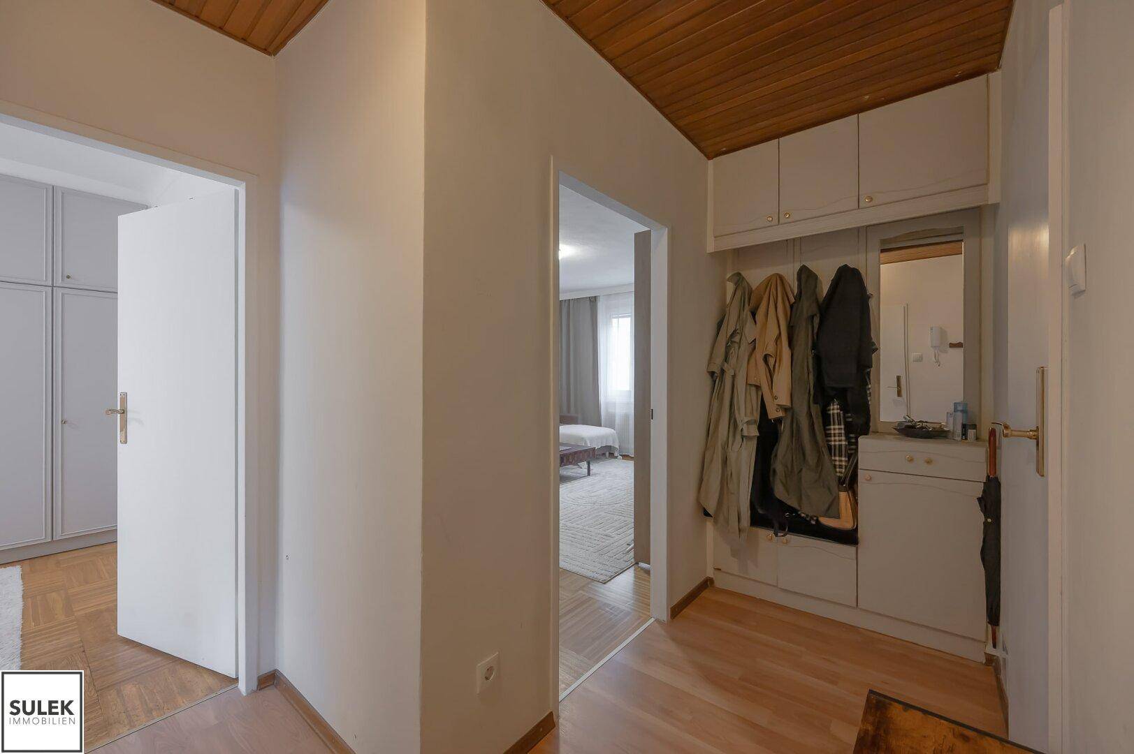 Heller Flur mit Garderobe, Spiegel und Holzdecke, verbindet verschiedene Wohnbereiche.