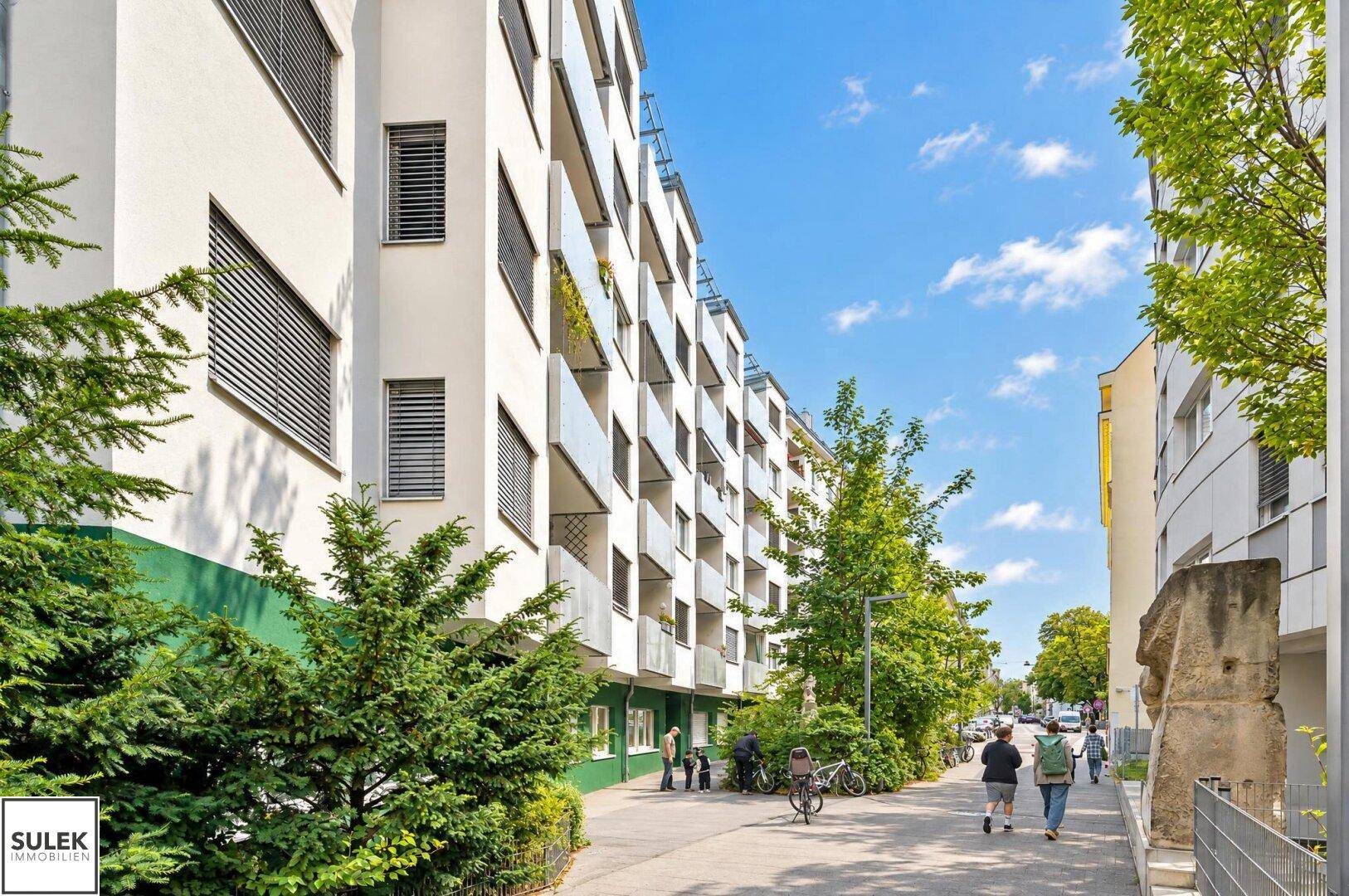 Moderne Wohngebäude mit Balkonen und grüner Umgebung entlang einer städtischen Straße.