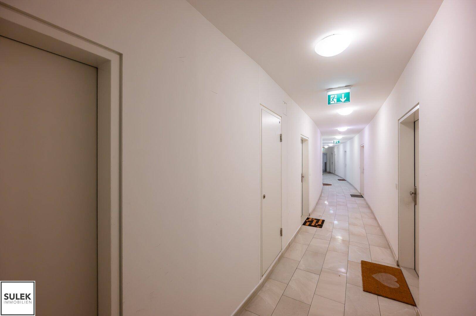 Langer, heller Flur mit Türen zu den Wohnungen und Fliesenboden.
