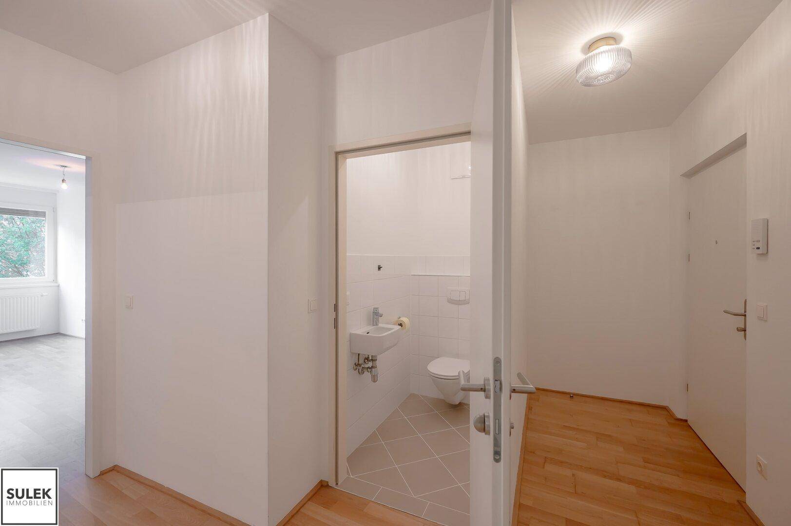 Heller Flur mit Holzboden und Zugang zu einem kleinen Gäste-WC mit Fliesenboden.