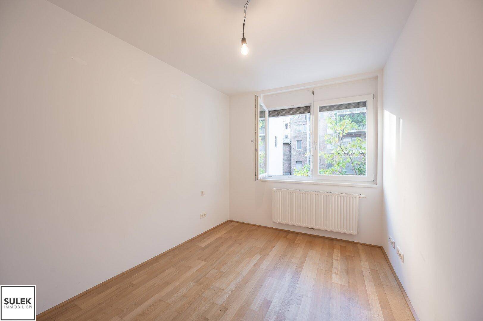 Helles Schlafzimmer mit Holzboden und einem Fenster, das viel natürliches Licht bietet.