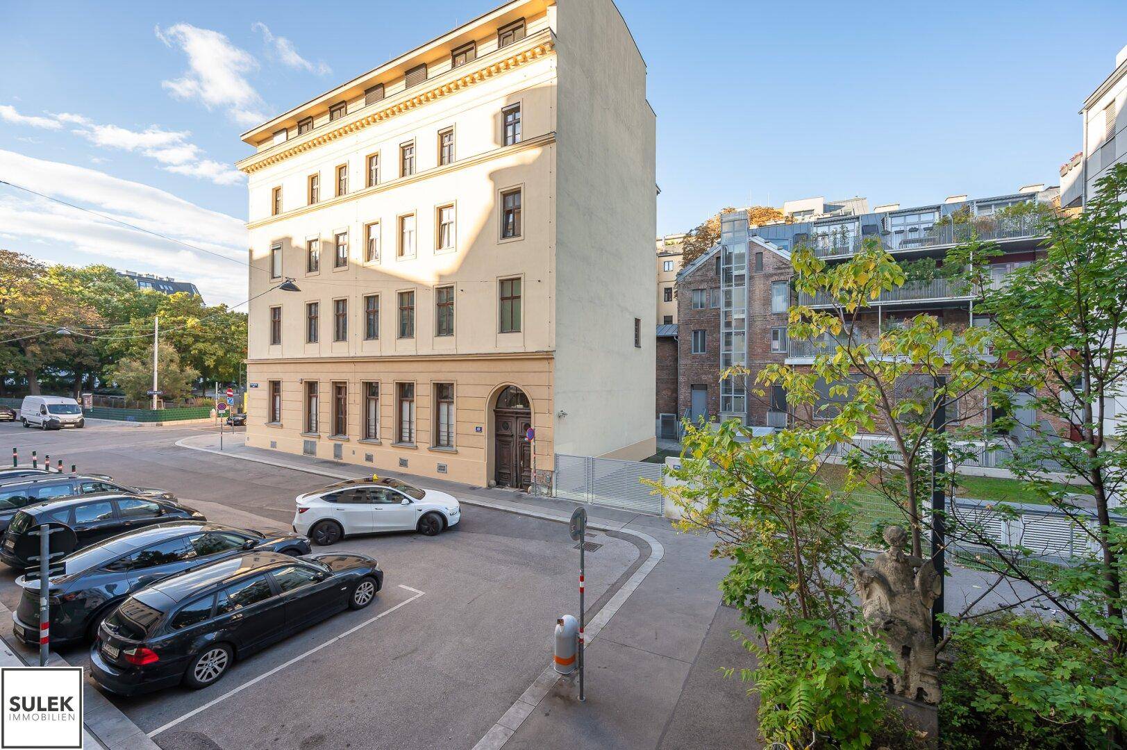 Historisches Gebäude mit klassischer Fassade und parkenden Autos auf der Straße.
