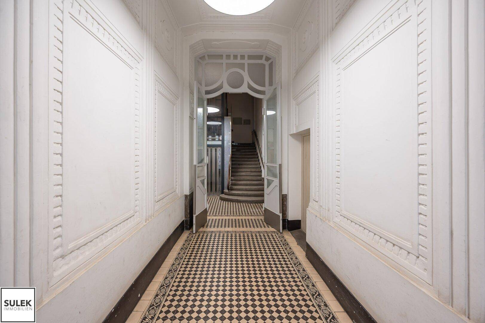 Prunkvoller Eingangsbereich eines Altbaus mit gemusterten Fliesen, verzierten Wänden und einer eleganten Treppe.