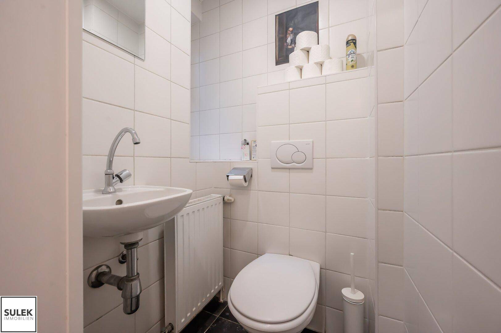 Kleines Gäste-WC mit weißem Waschbecken, Toilette und weißen Fliesen, funktional eingerichtet.