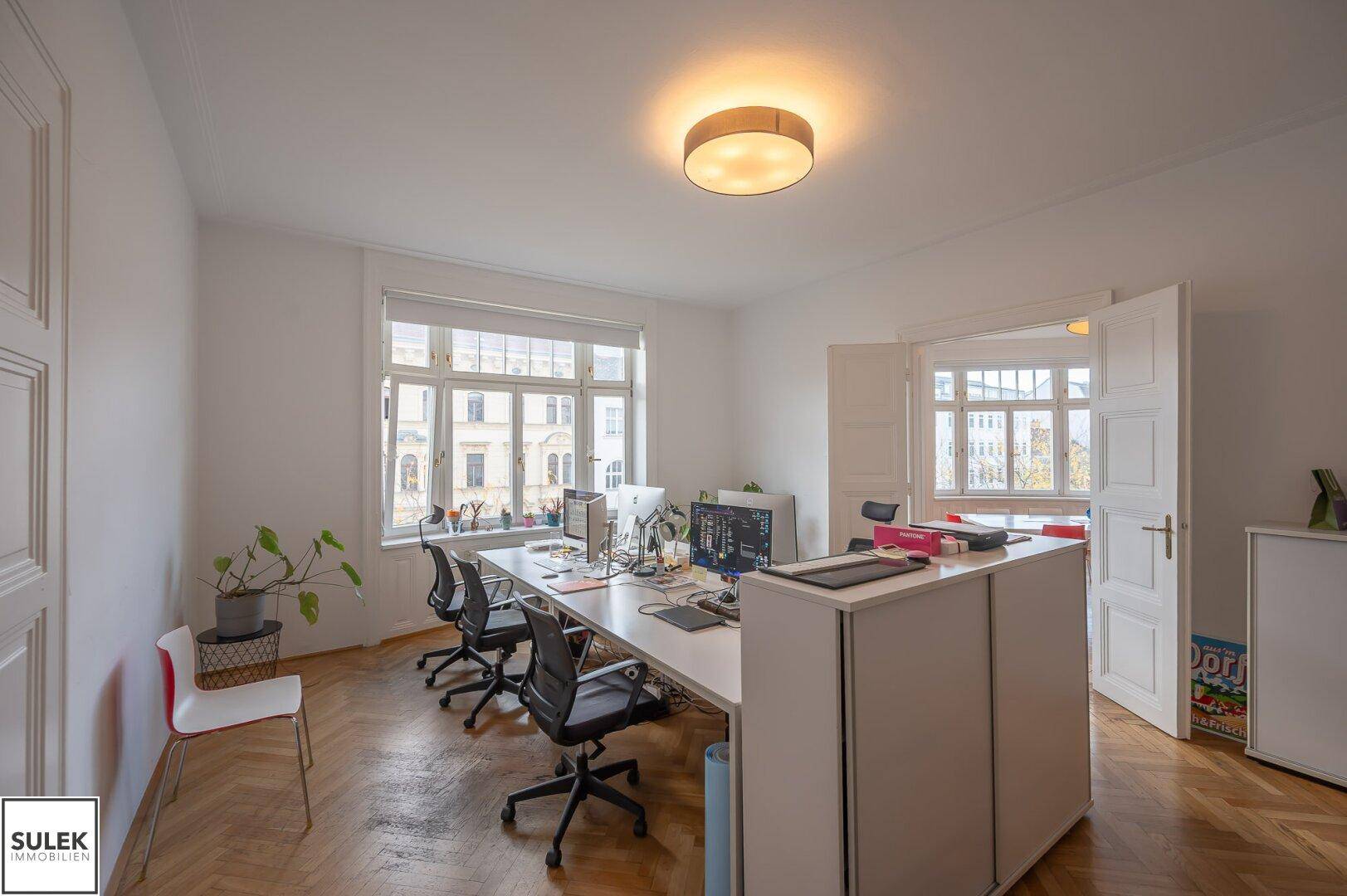 Geräumiges Büro mit mehreren Schreibtischen, viel Tageslicht und traditionellem Fischgrätparkett.