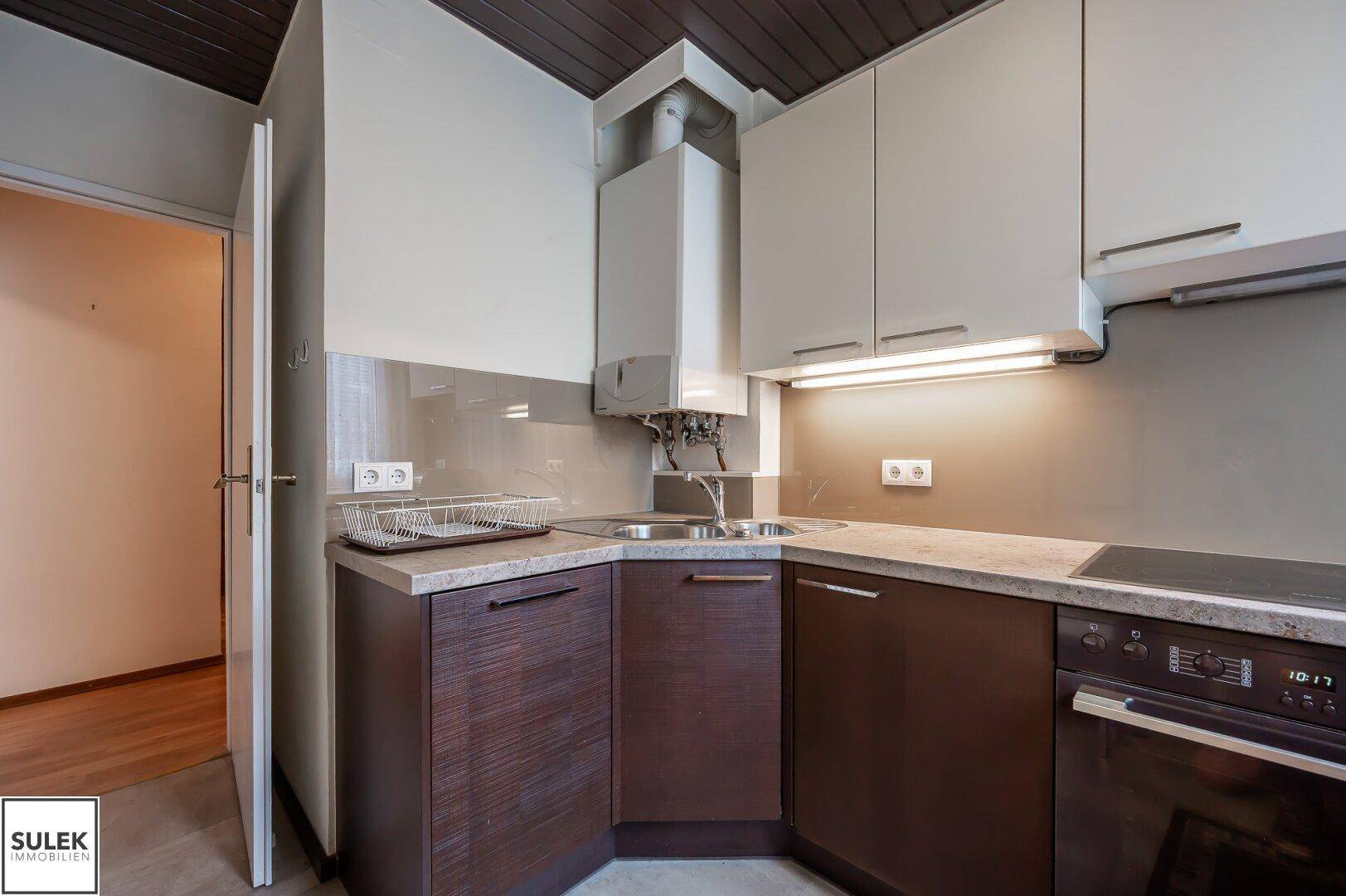 Praktische Küche mit Spüle, Backofen und sichtbarem Warmwasserboiler unter Holzdecke.