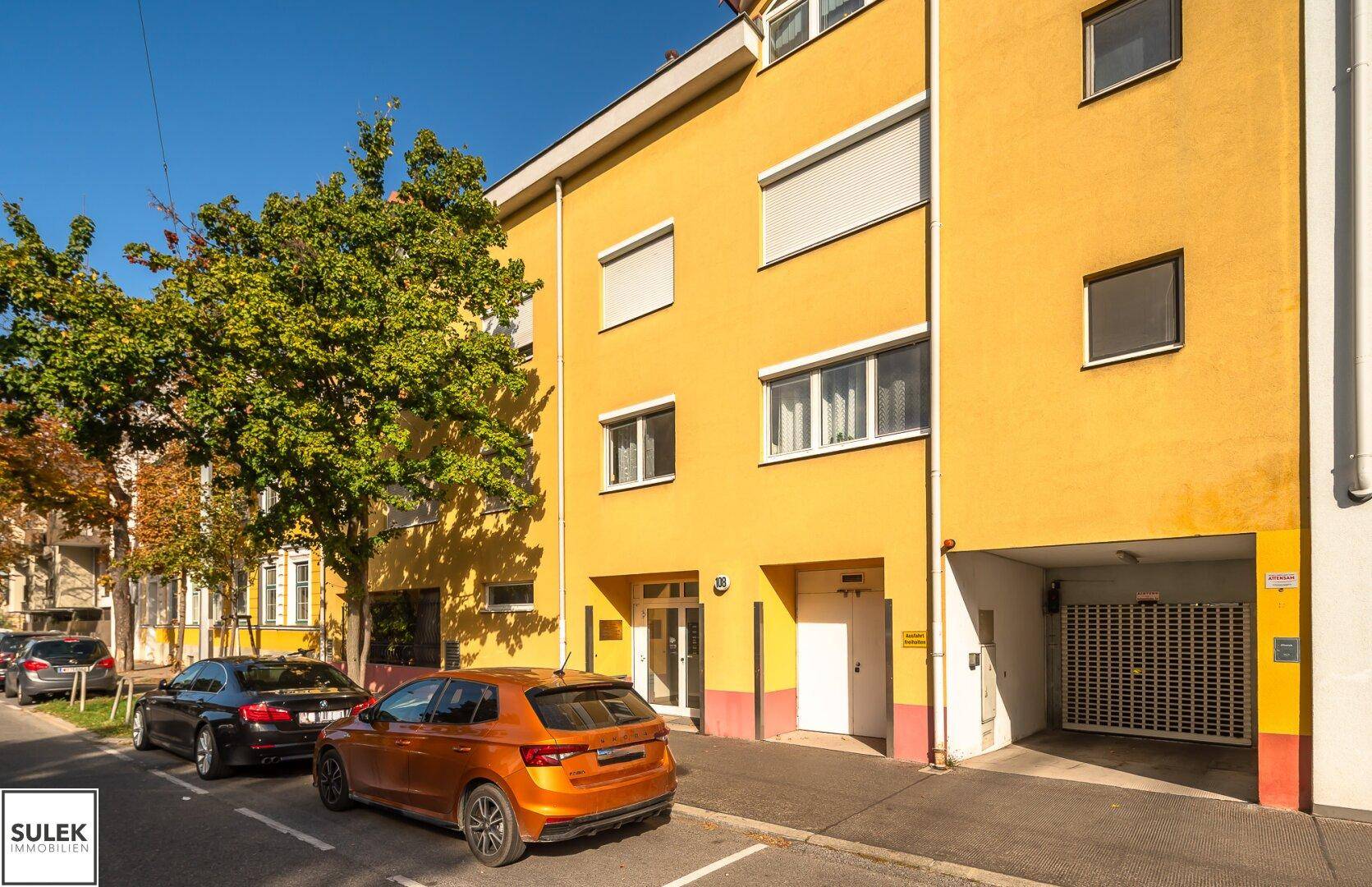 Ansicht der gelben Gebäudefassade mit Einfahrt zur Tiefgarage.